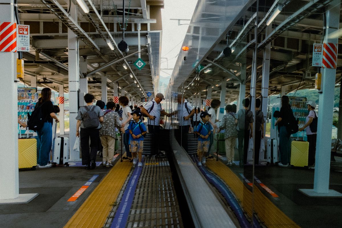 Passeggeri sulla banchina riflessi nel finestrino del treno, ai piedi del Fuji
