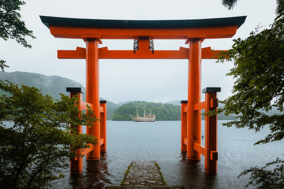 Il torii rosso sul lago Ashi nella pioggia, con la nave all’orizzonte, Hakone