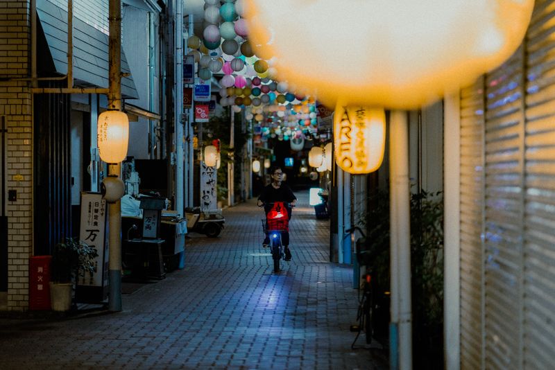 Ciclista in fondo a una galleria commerciale addobbata di lanterne di carta colorate, al crepuscolo, Kyoto