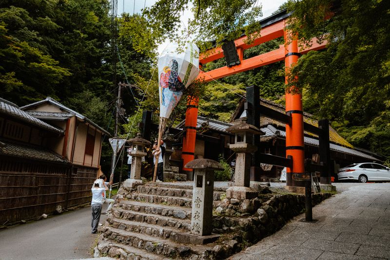 Alcune persone issano una grande lanterna di carta davanti al torii vermiglio di Atago, Toriimoto, Kyoto