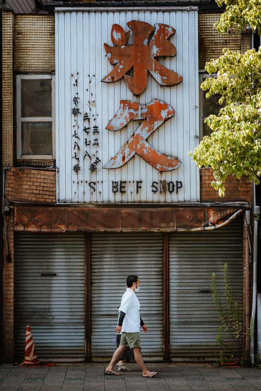 Uomo cammina sotto la vecchia insegna arrugginita di un negozio chiuso, Kyoto