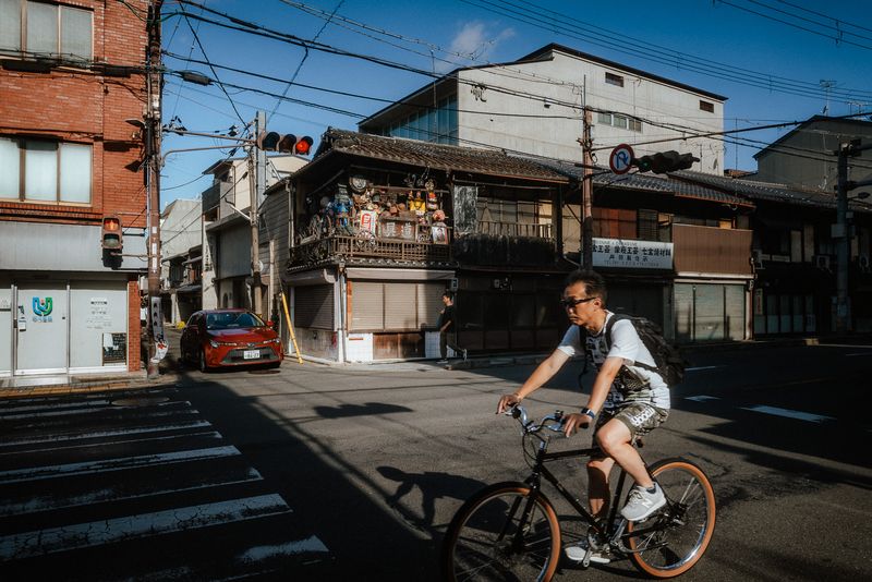Uomo in bicicletta passa davanti a un vecchio negozio d'angolo pieno di oggetti, Kyoto