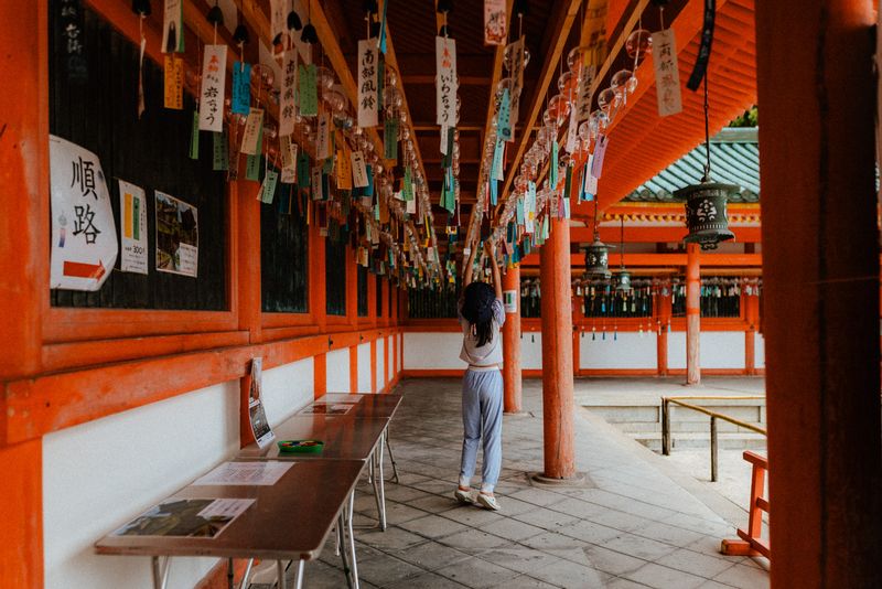 Bambina si allunga verso i campanelli di vetro (fūrin) sotto il portico vermiglio di un santuario, Kyoto