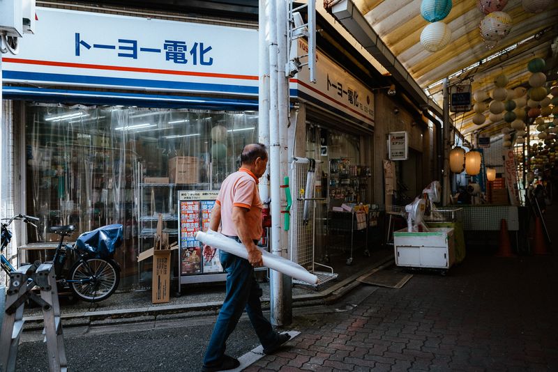 Commerciante che attraversa la strada con un rotolo di pellicola davanti a un negozio di elettrodomestici, Kyoto