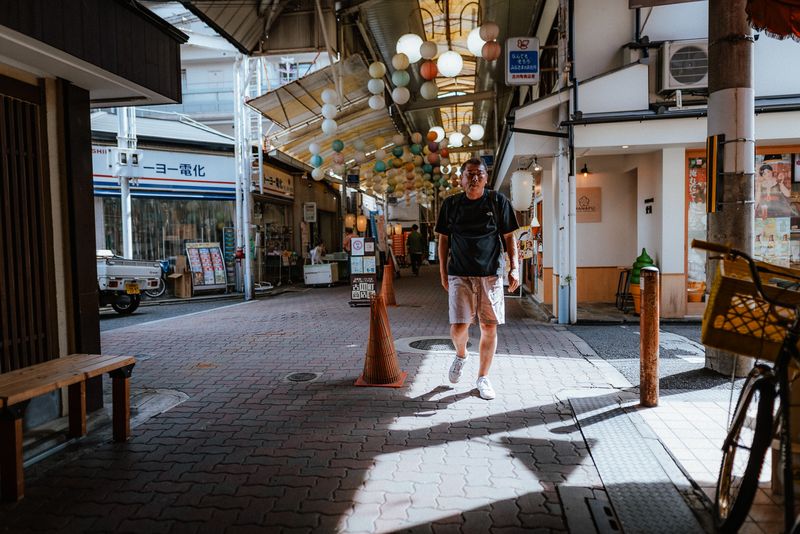 Uomo che cammina nel taglio di luce della galleria commerciale Furukawachō sotto le lanterne di carta, Kyoto