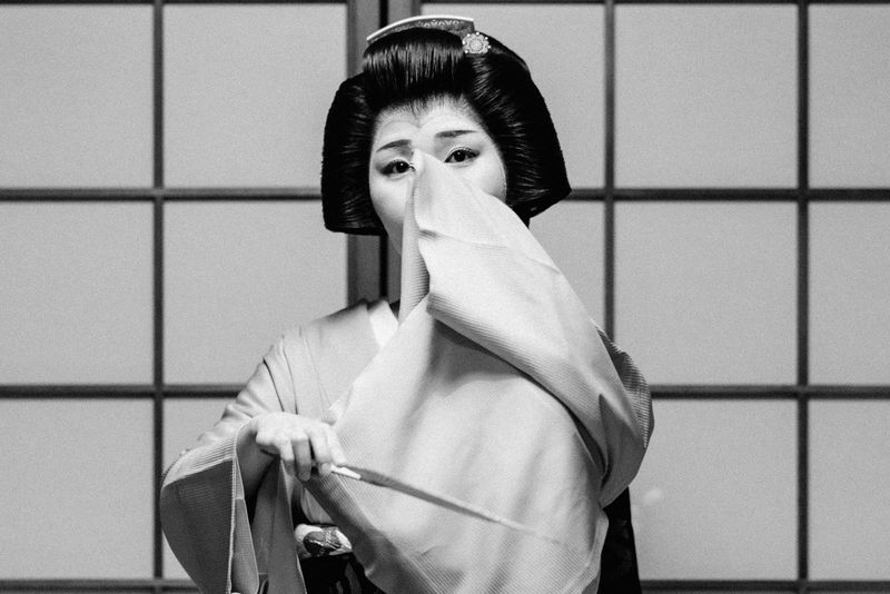 Ritratto in bianco e nero di una geiko che si copre il volto con un telo di seta, Kyoto