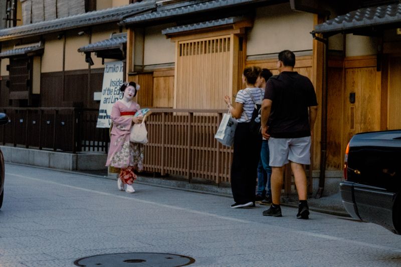 Una maiko in kimono rosa passa accanto ad alcuni turisti in una via di Gion, Kyoto