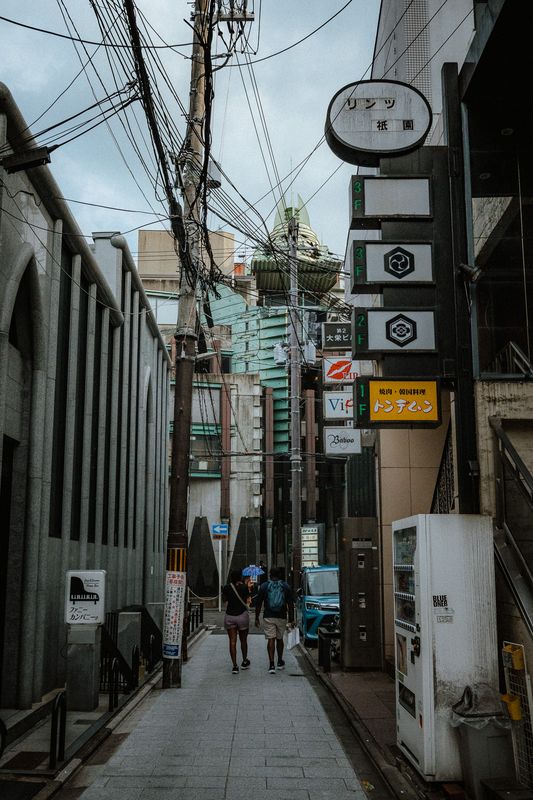 Coppia con ombrello cammina in un vicolo di Gion tra le insegne verticali, Kyoto