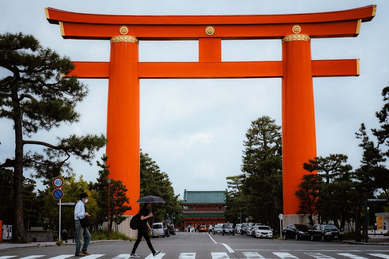 Il grande torii vermiglio di Heian Jingū con un uomo e una figura con l'ombrello alle strisce, Kyoto