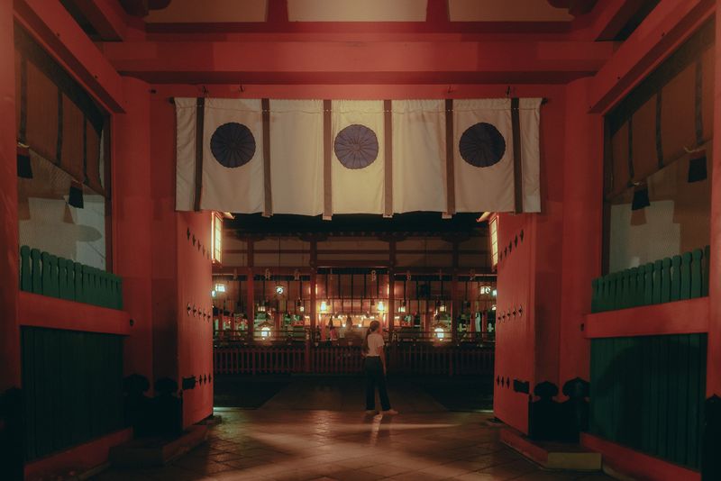 Figura sotto i noren con lo stemma del crisantemo all'ingresso di Fushimi Inari, di notte, Kyoto
