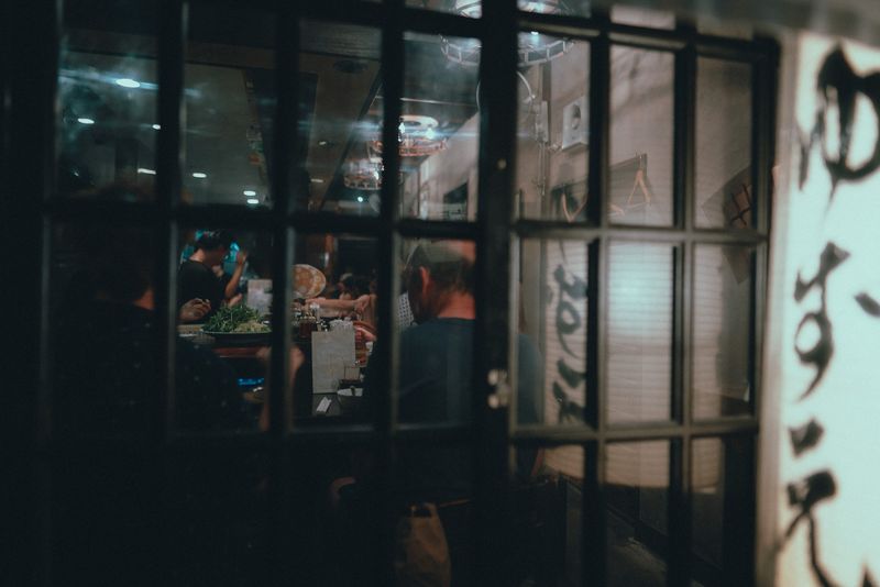 Avventori di un izakaya visti attraverso la vetrata a riquadri accanto a una lanterna, di notte, Kyoto