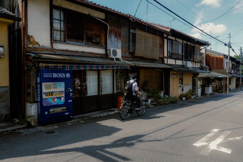 Ciclista lungo una via di vecchie machiya con un distributore automatico Suntory Boss, Kyoto