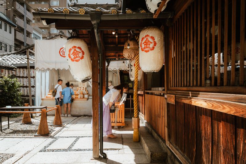 Donna si inchina sotto le lanterne dorate del santuario del denaro Mikane, Kyoto