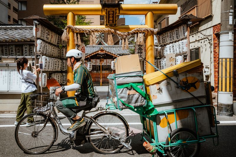 Un corriere in bicicletta passa davanti al torii dorato del santuario Mikane, Kyoto
