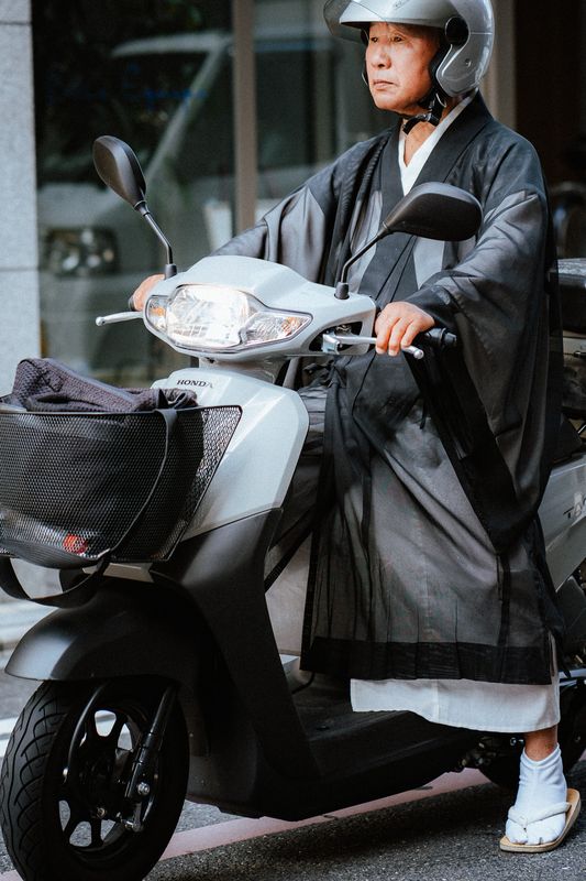 Un monaco buddhista in abito e casco su uno scooter Honda con i tabi ai piedi, Kyoto