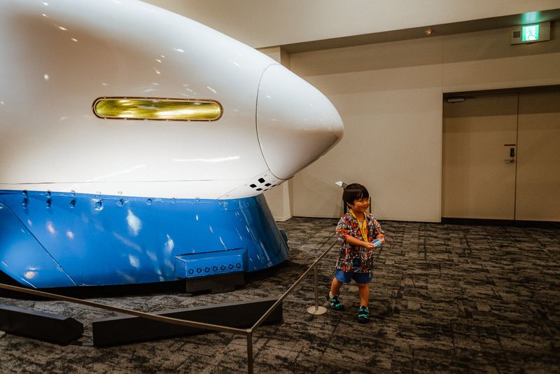 Bambino sorridente accanto al muso di uno Shinkansen 0 al museo ferroviario, Kyoto