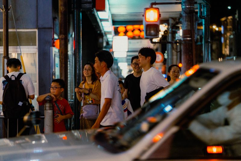 Piccola folla a un angolo di strada tra lanterne e semaforo rosso, di notte, Kyoto