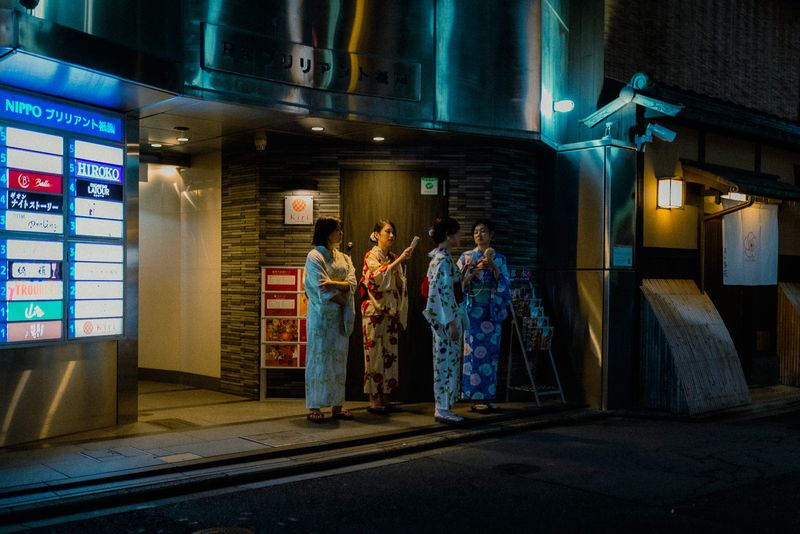 Quattro donne in yukata chiacchierano sotto le insegne al neon, di notte a Gion, Kyoto