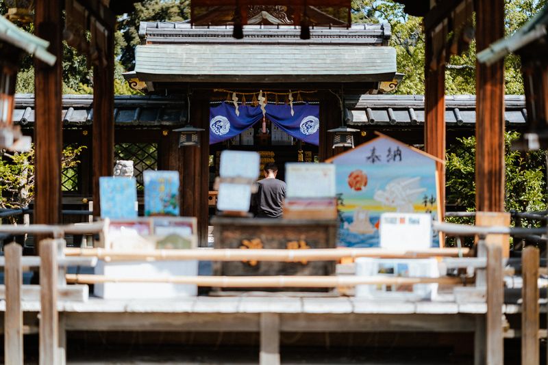 Uomo in preghiera davanti al noren blu di un santuario tra le tavolette ema, Kyoto