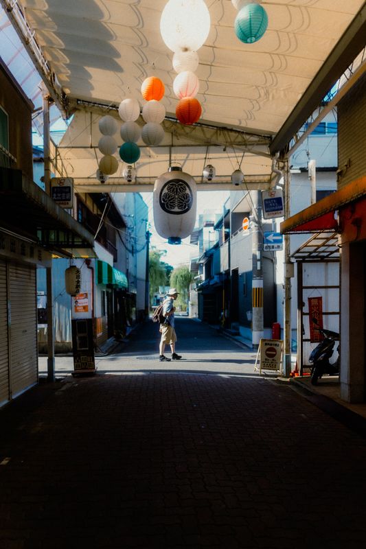 Uomo attraversa la luce in fondo a una galleria commerciale addobbata di lanterne di carta colorate, Kyoto