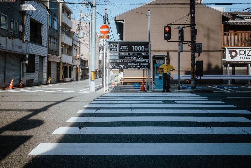 Un parcheggiatore in maglia gialla in attesa oltre le strisce pedonali, Kyoto