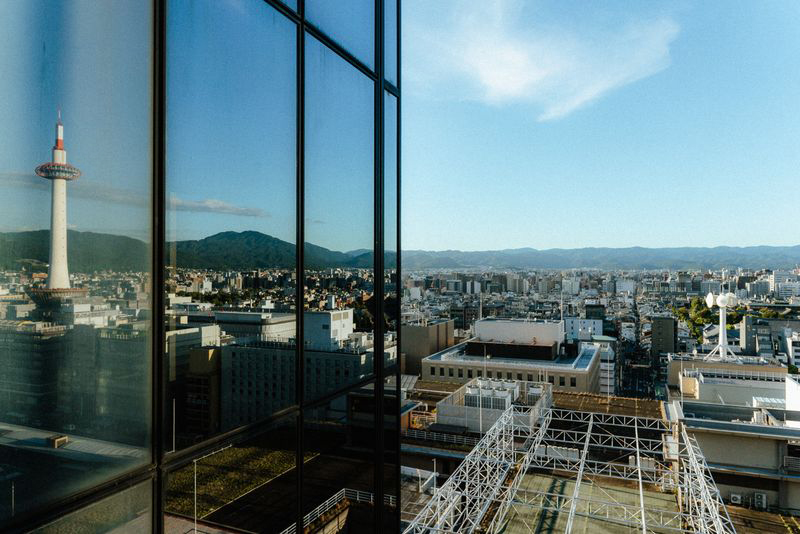 La Kyoto Tower riflessa nel vetro di un edificio con la città e i monti sullo sfondo, Kyoto