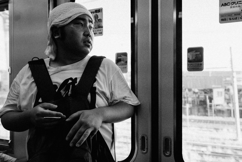 Uomo con un asciugamano sul capo guarda fuori dal finestrino di un treno, in bianco e nero, Kyoto