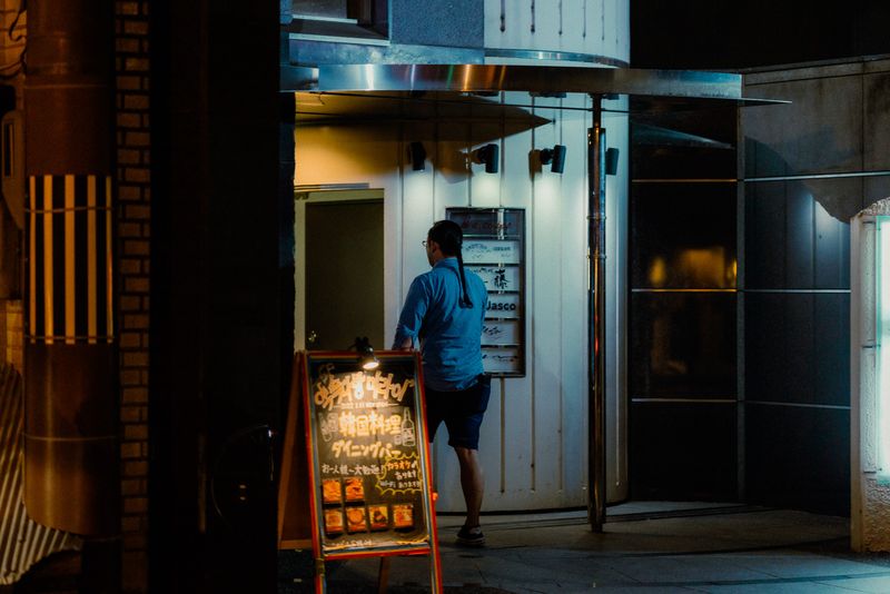 Uomo legge la lavagna del menù di un locale illuminato, di notte, Kyoto