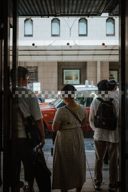 Persone in attesa dietro una porta a vetri con il riflesso di un palazzo, Kyoto