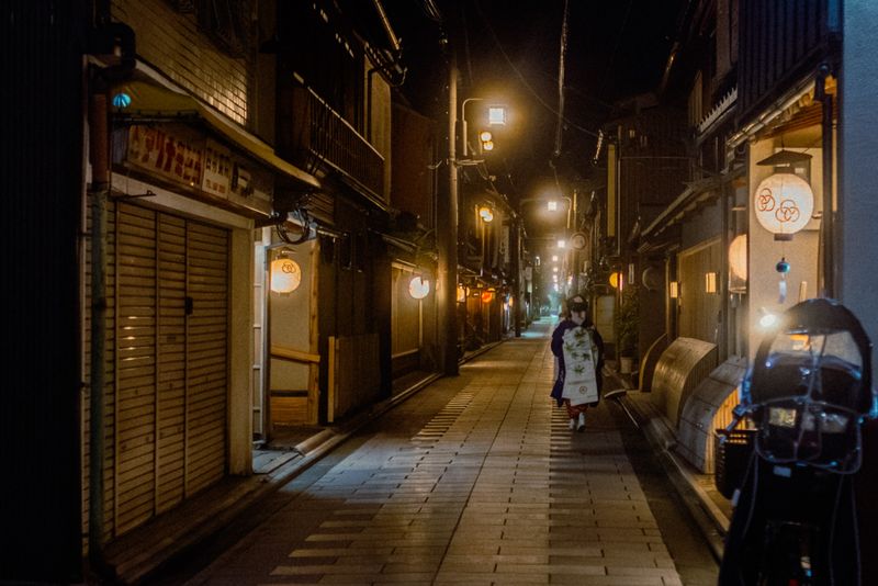 Una maiko si allontana in un vicolo di lanterne rotonde, di notte, Kyoto