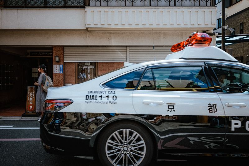 Un'auto della polizia di Kyoto sfreccia davanti a una donna in attesa sul marciapiede, Kyoto
