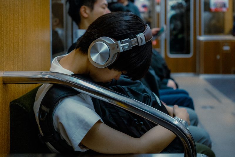 Ragazzo addormentato con le cuffie appoggiato al corrimano di un vagone, in viaggio verso Nachi