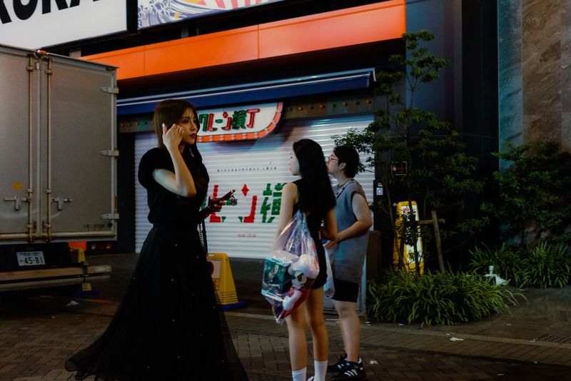 Donna in abito nero lungo al telefono davanti a una serranda abbassata, di notte, Osaka
