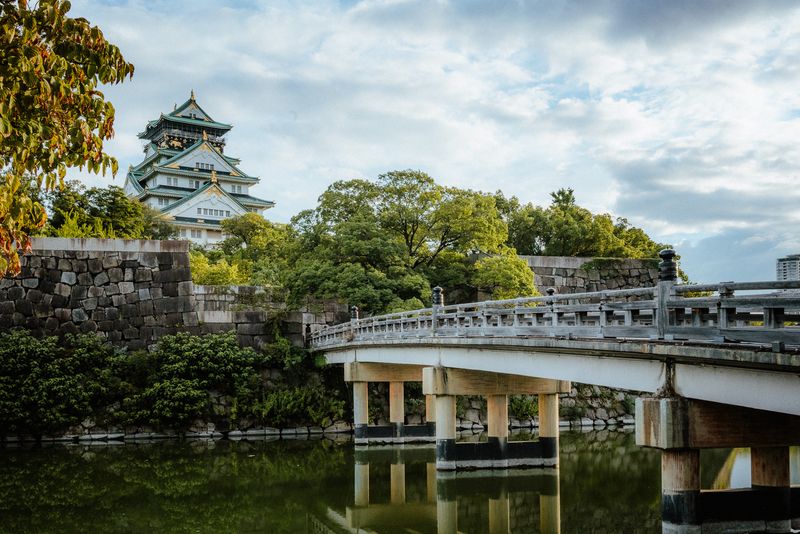 Il castello di Osaka oltre il ponte e le mura di pietra del fossato, luce del tardo pomeriggio, Osaka