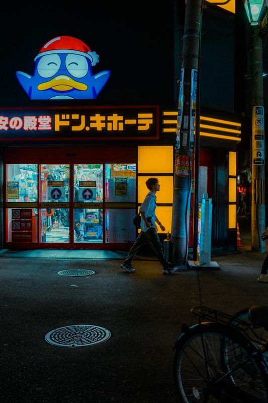 Passante che attraversa l'angolo davanti all'insegna al neon di Don Quijote, di notte, Osaka
