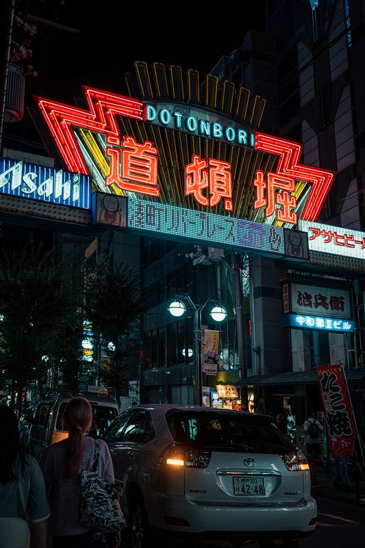 La grande insegna al neon di Dōtonbori sopra il traffico e i passanti, di notte, Osaka