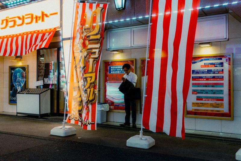 Uomo al telefono tra le bandiere a righe rosse e bianche davanti al Grand Chateau, Osaka