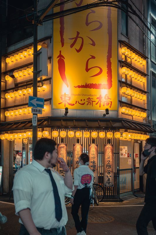 Angolo di un locale tappezzato di lanterne gialle a Higashi-Shinsaibashi, passanti in primo piano, Osaka