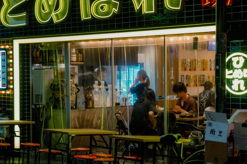 Avventori di un izakaya dietro le tende di plastica sotto l'insegna al neon verde, Osaka