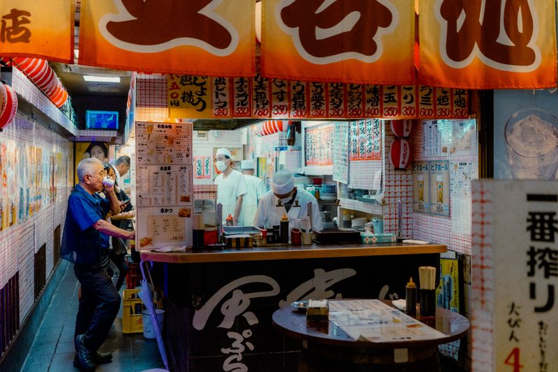 Cuochi in divisa bianca dietro il bancone di un locale di kushikatsu tappezzato di menù, Osaka