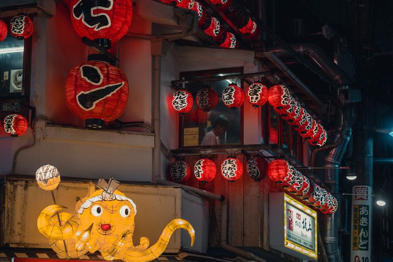 Cascata di lanterne rosse e insegna luminosa a forma di polpo, una figura alla finestra, Osaka