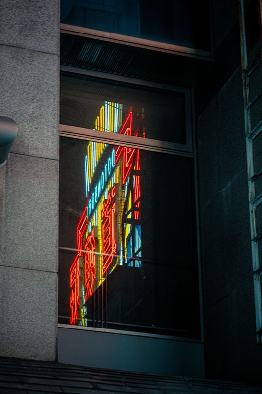 Insegna al neon rossa e gialla riflessa nella vetrata di un palazzo in cemento, Osaka