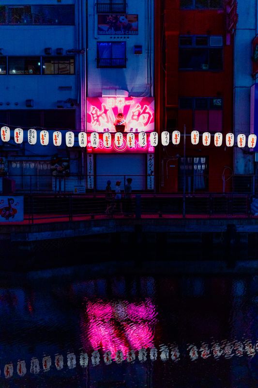 Insegna al neon rosa e fila di lanterne riflesse nell'acqua scura del canale, Osaka