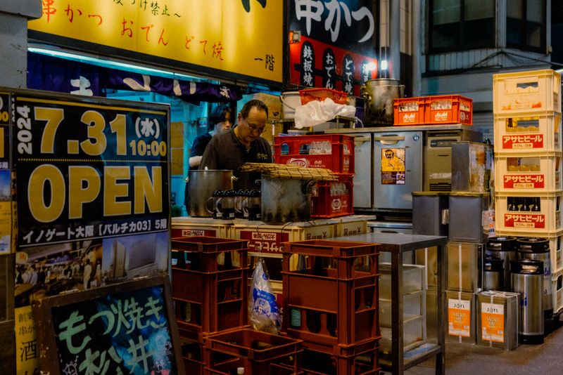 Cuoco al lavoro tra le casse di birra impilate del retro di un locale di kushikatsu e oden, Osaka