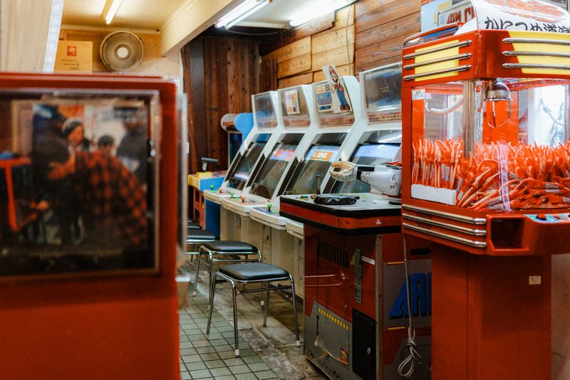 Fila di cabinati anni Ottanta e gru pescapremi in una sala giochi d'epoca, Osaka
