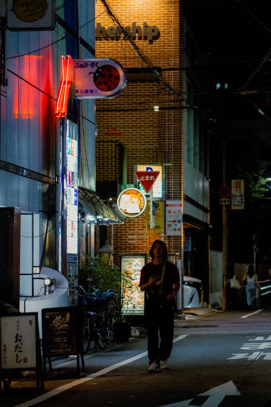 Uomo che cammina in una via laterale sotto l'insegna al neon con la coccinella, Higashi-Shinsaibashi, Osaka