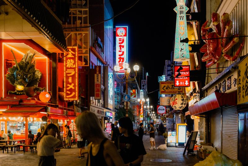 La strada di Shinsekai di notte tra il drago del Kinryū, il granchio meccanico e le insegne al neon, Osaka