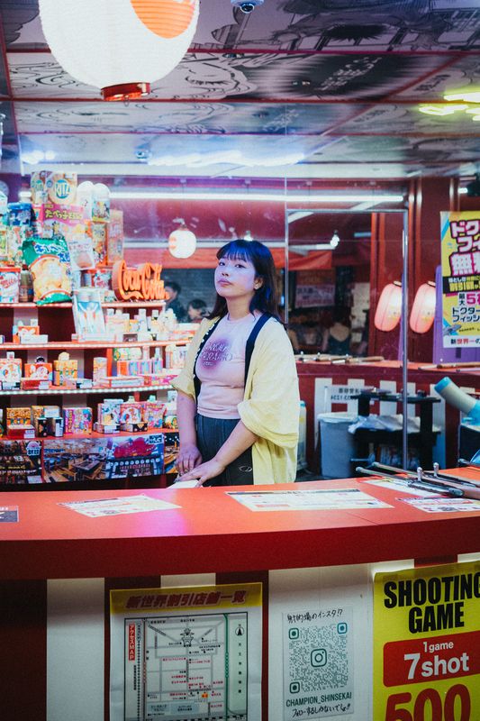 Ragazza al banco di un tiro a segno tra dolciumi e luci al neon, Shinsekai, Osaka