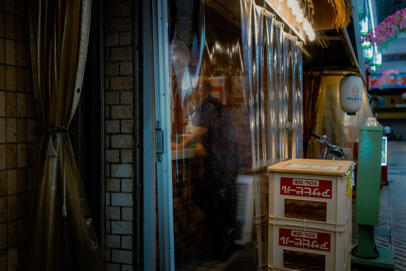 Sagoma di un uomo al lavoro dietro una tenda di plastica accanto alle casse di birra impilate, Osaka