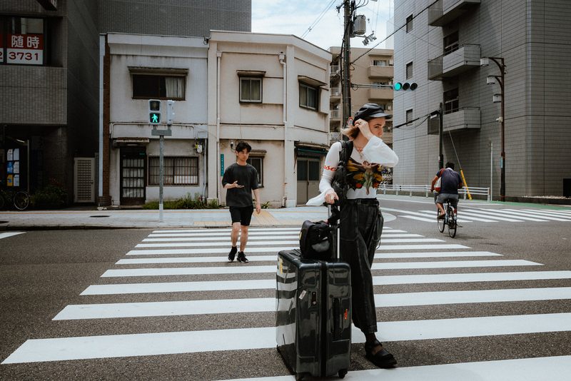 Donna con trolley si sistema i capelli sulle strisce pedonali, Osaka